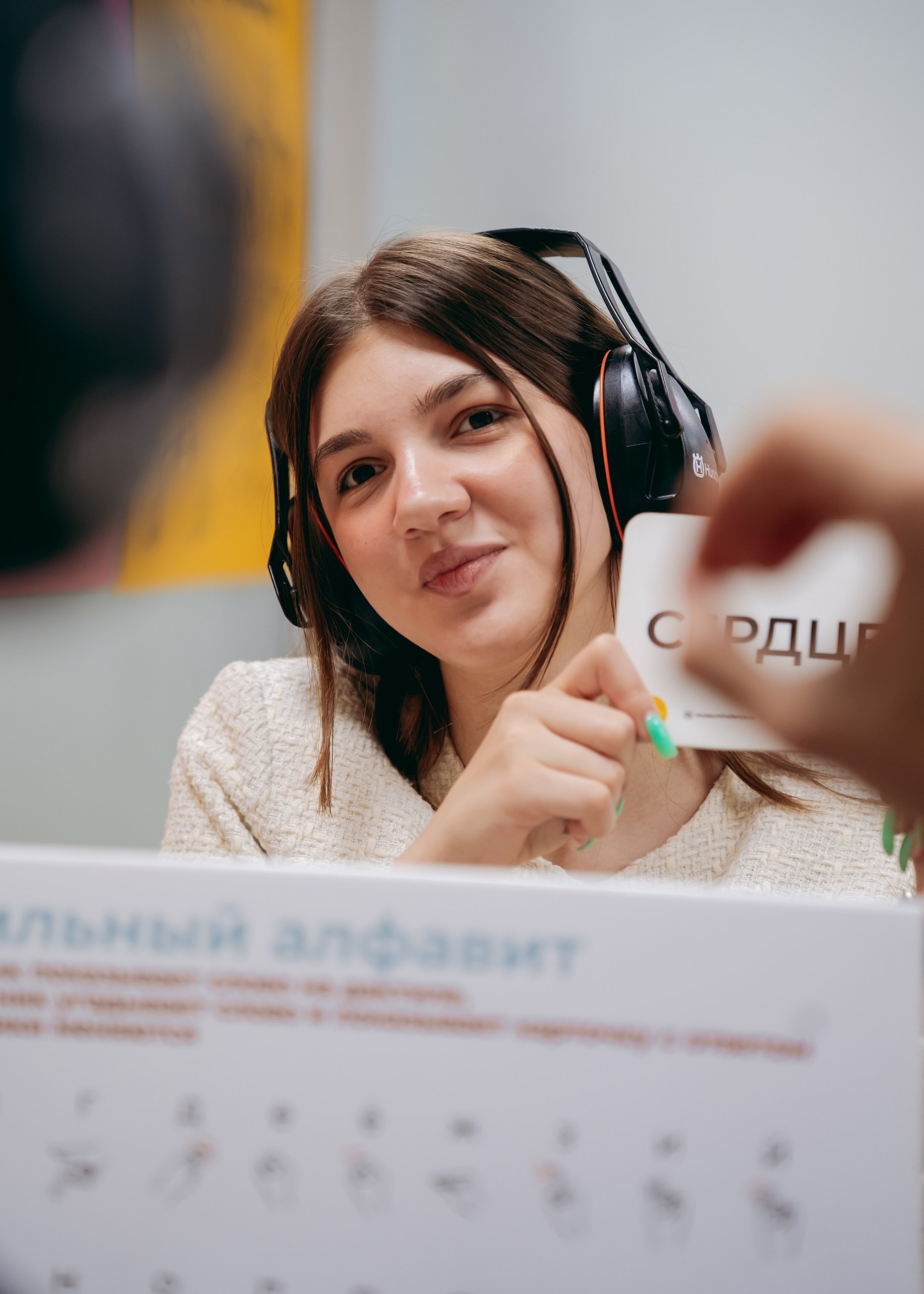 Участница экскурсии в наушниках держит карточку со словом «Сердце»